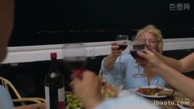 在户外阳台上吃晚饭时，年长的妇女举杯祝酒，家庭成员碰杯喝酒